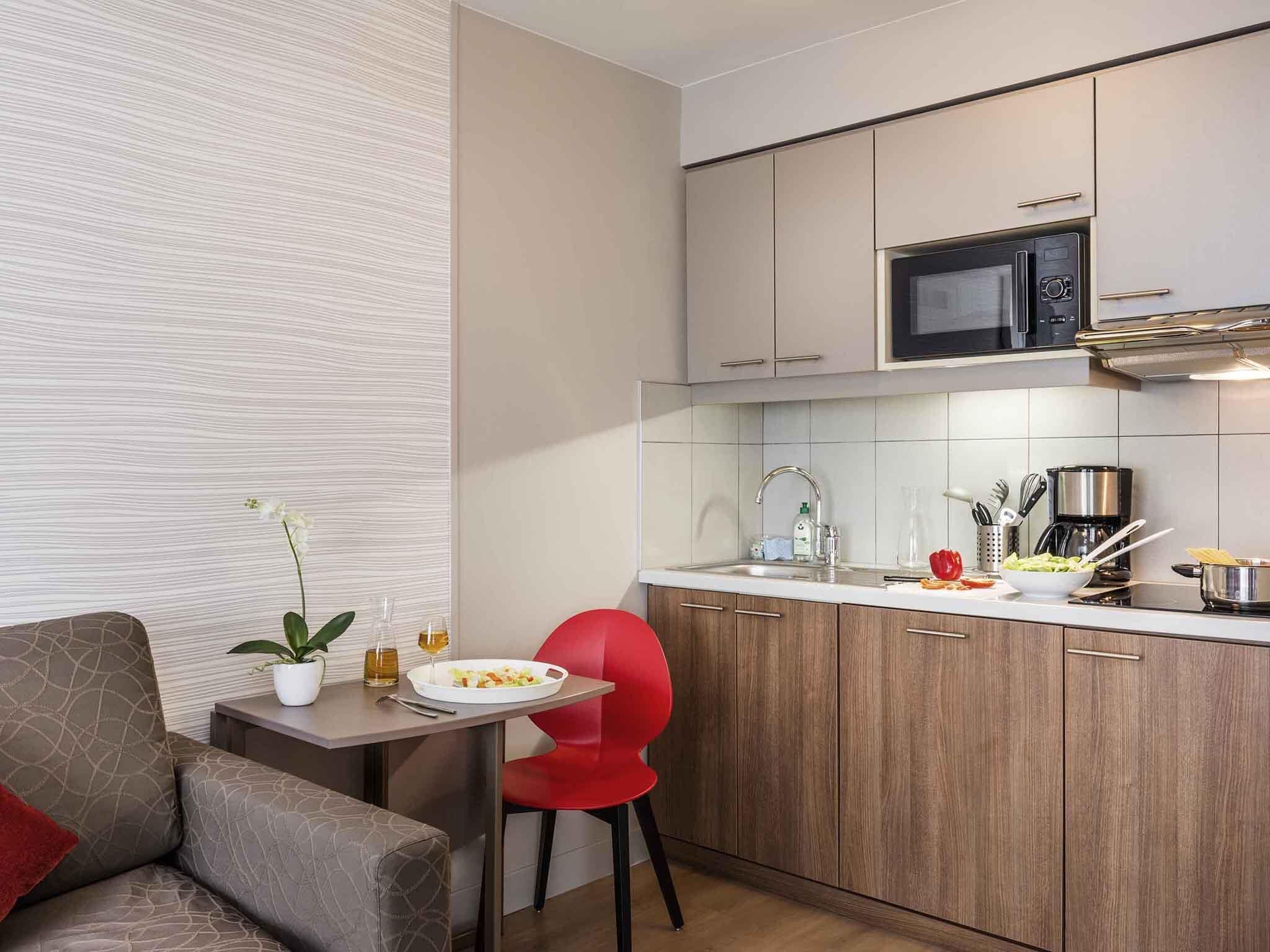 A compact kitchen with a microwave, coffee maker, and a small dining area with a red chair and a table.