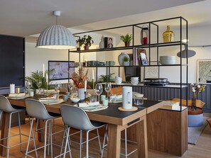 Een moderne keuken met een houten eettafel, barkrukken, een hanglamp en een metalen rek met diverse spullen.