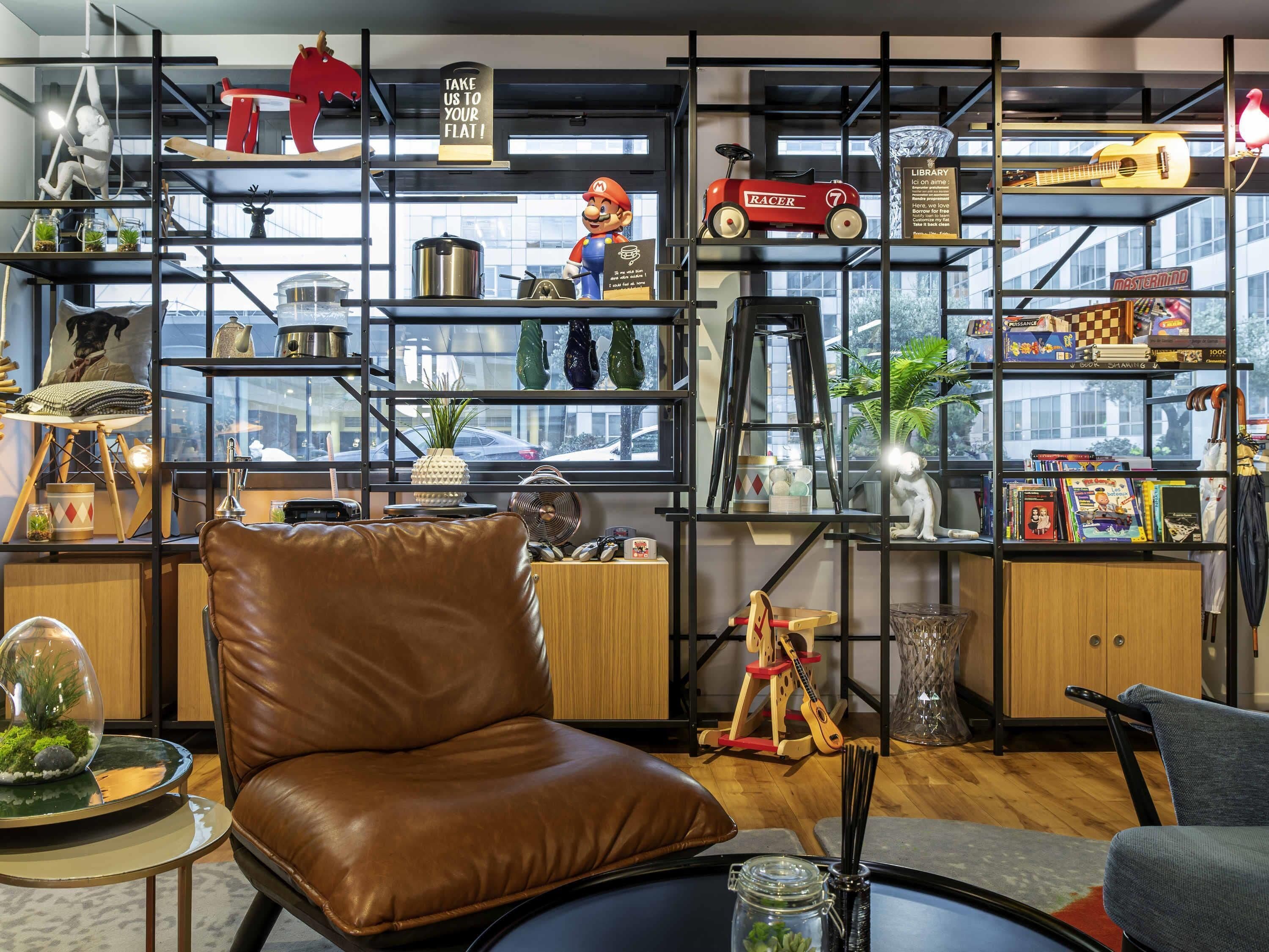 A modern living room with a brown leather chair, a glass coffee table, and a bookshelf filled with various items including a Mario figurine, a toy car, and board games.