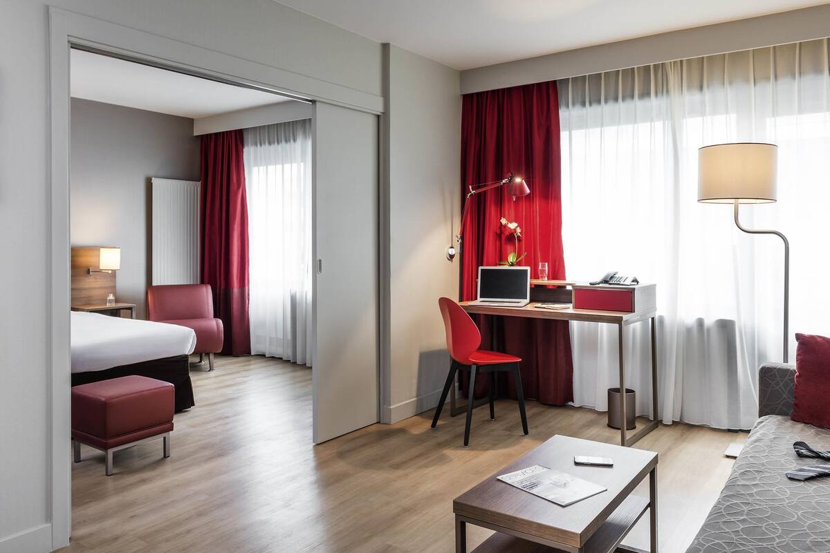 Een hotelkamer met een bed, bureau, computer, stoel en een klein tafeltje met een lamp.