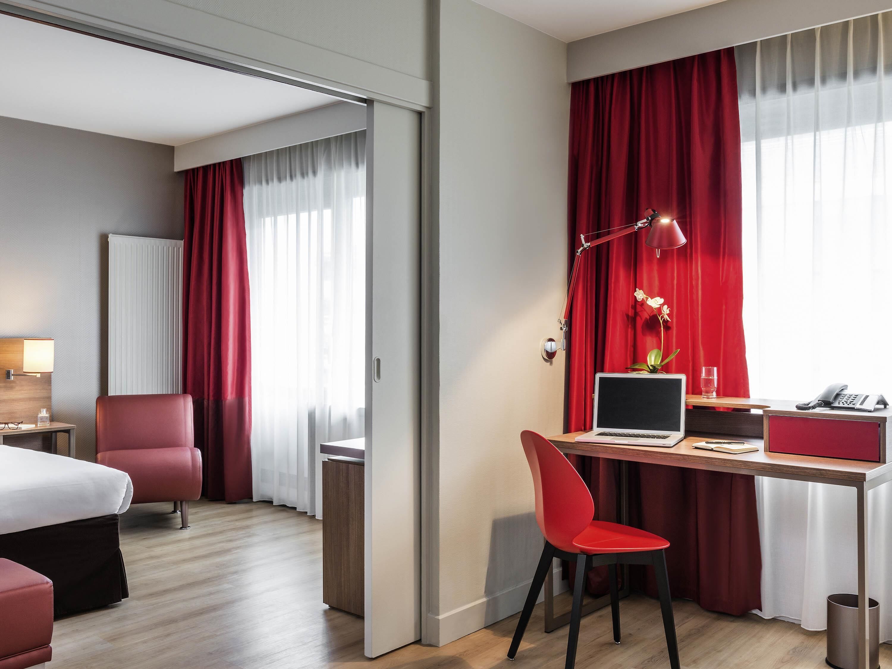 Habitación de hotel con cama, escritorio, laptop, silla, lámpara y teléfono.