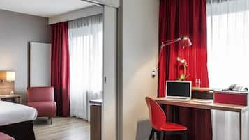 Habitación de hotel con cama, escritorio, laptop, silla, lámpara y teléfono.