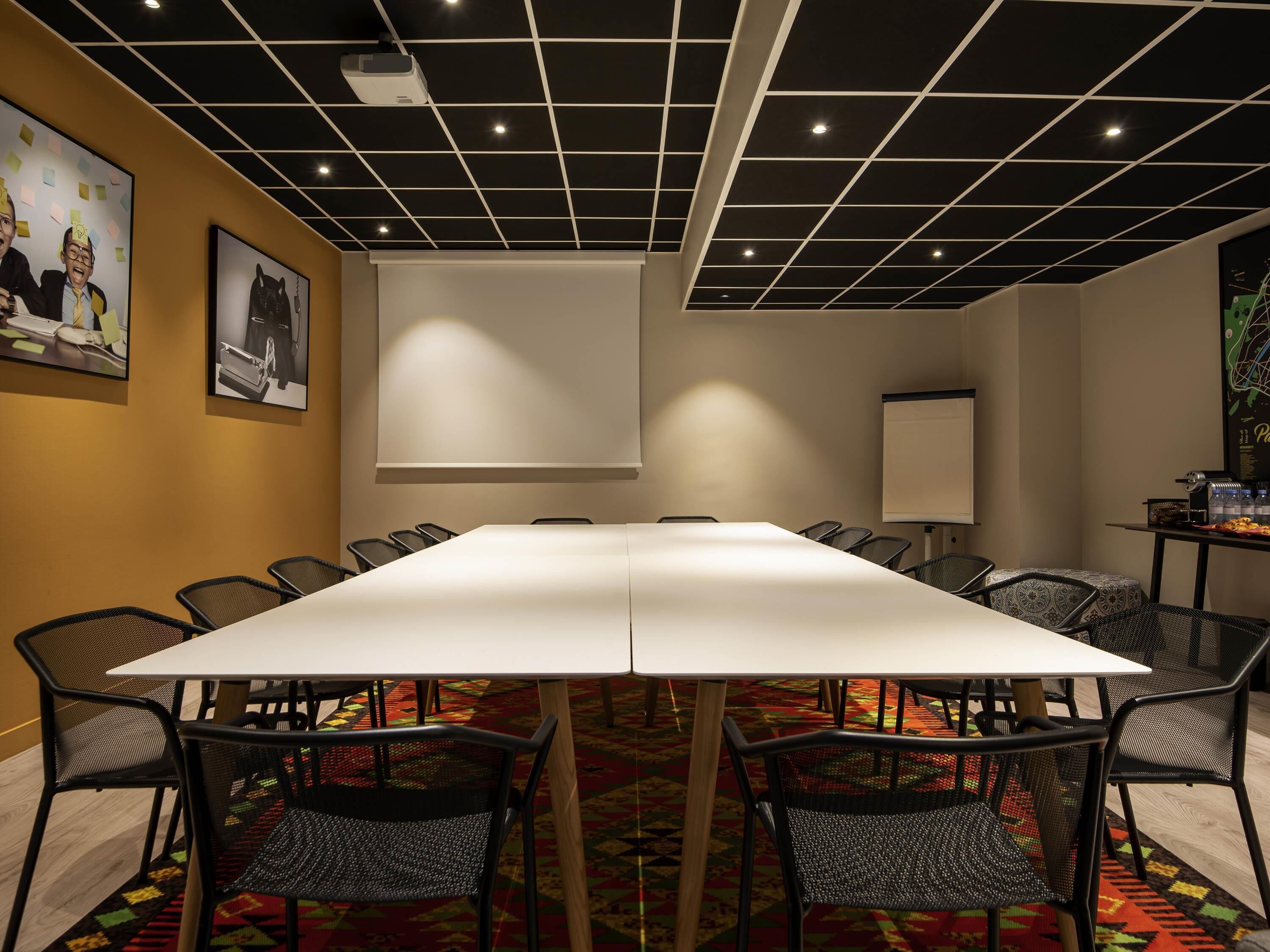 A conference room with a long table, black mesh chairs, a projector, and a white screen.