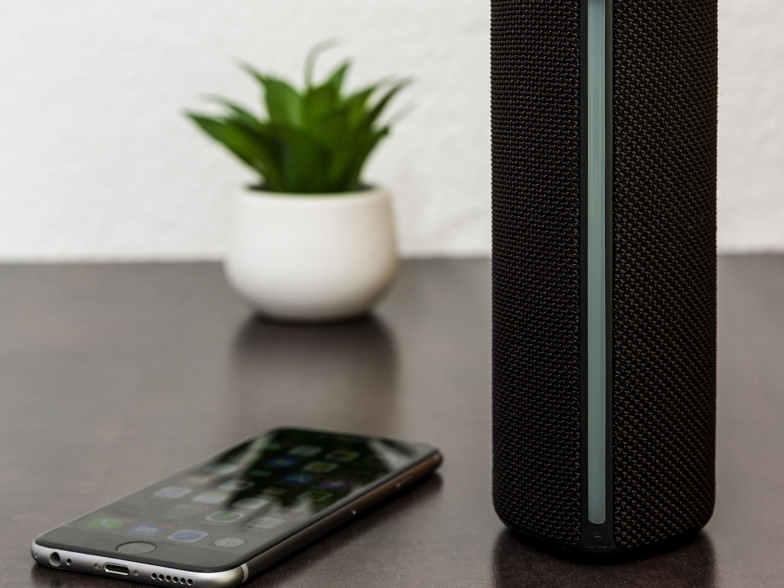 A smartphone on a table with a black speaker beside it.