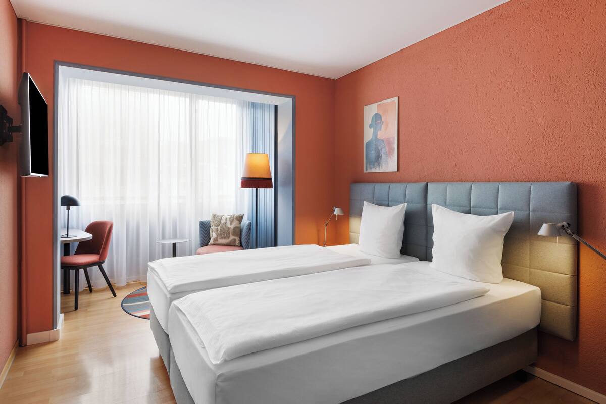 Habitación de hotel con dos camas, un escritorio, una silla y un televisor.