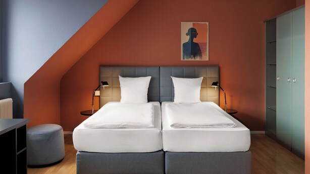 A bedroom with two beds, a headboard, bedside lamps, a wardrobe, and a painting on the wall. - Hotel La Pergola (Bern)