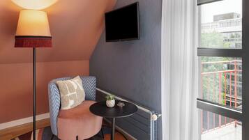 Una habitación acogedora con una silla moderna, una mesita pequeña, una lámpara de pie y un televisor fijado a la pared.