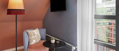 A cozy room with a modern chair, a small table, a floor lamp, and a TV mounted on the wall.