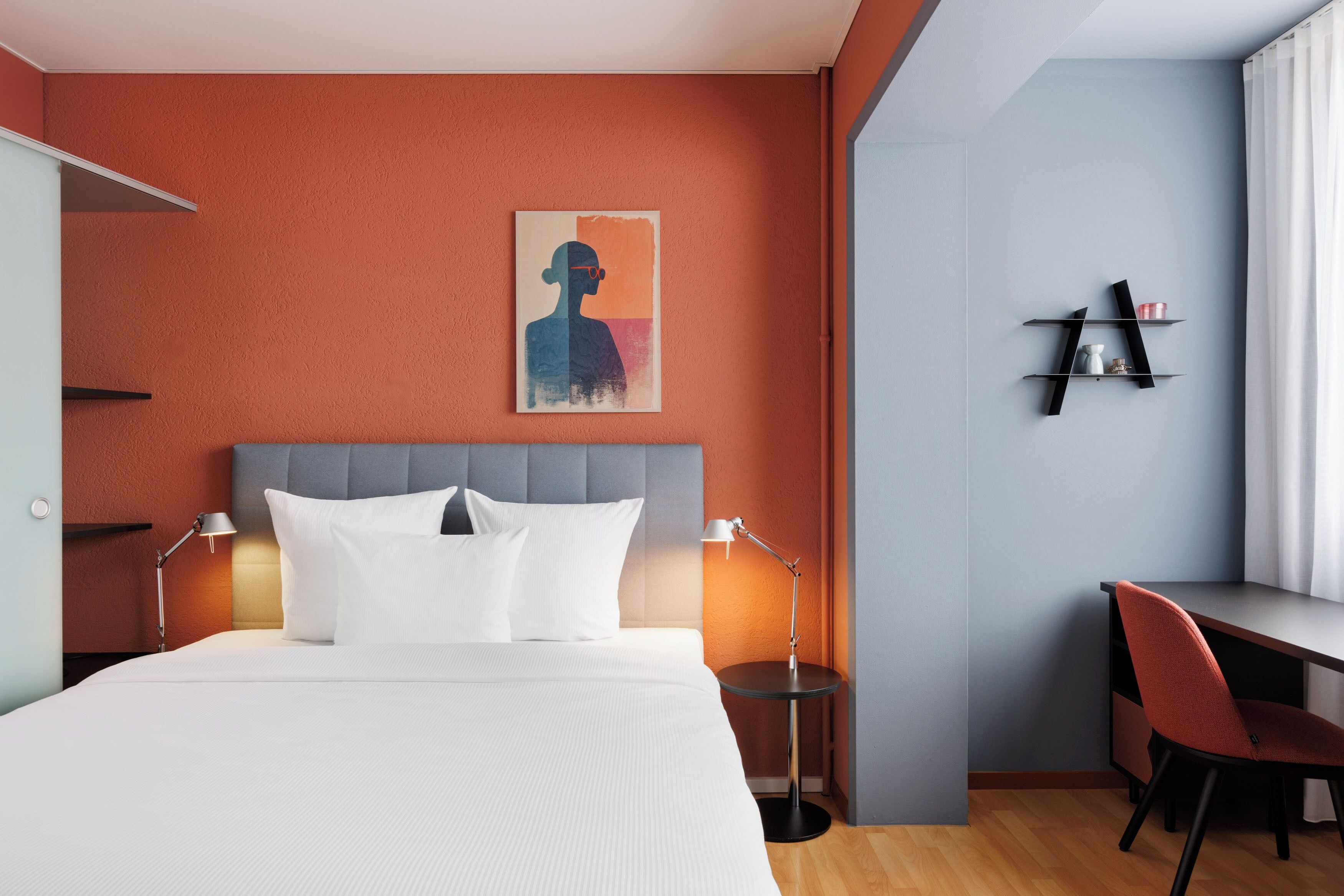 Une chambre d’hôtel avec un lit, des lampes de chevet, un bureau et une chaise.