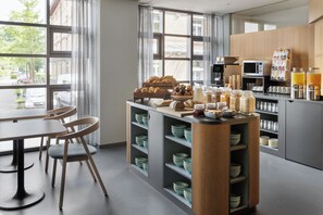A modern kitchen with a breakfast bar, wooden chairs, and a variety of breakfast items. - Hotel La Pergola (Bern)