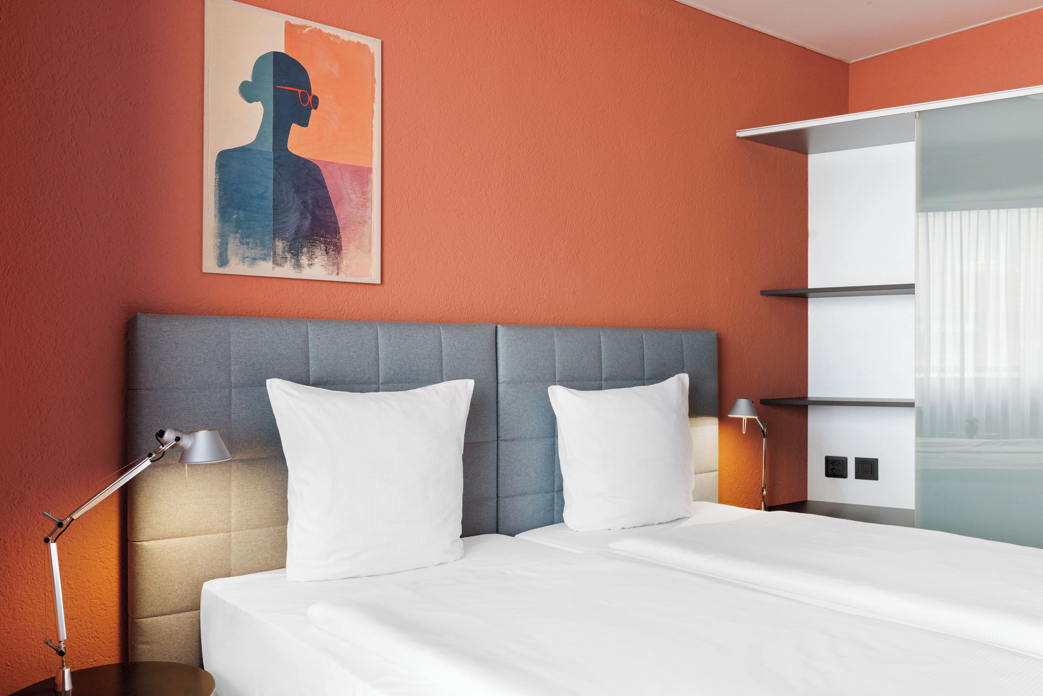 Une chambre d’hôtel avec un lit, une table de chevet, une lampe, un tableau au mur et une porte coulissante de placard.