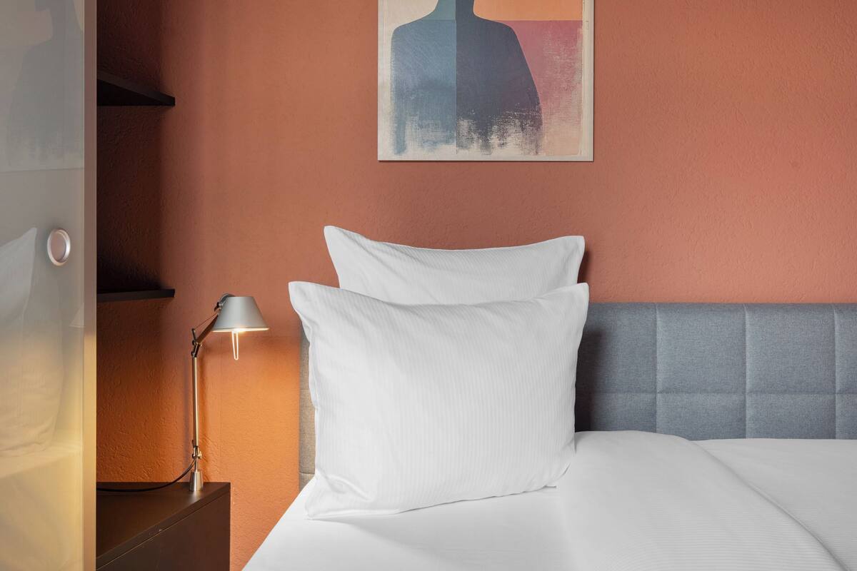 Una habitación de hotel con una cama, una mesita de noche, una lámpara y un cuadro en la pared.