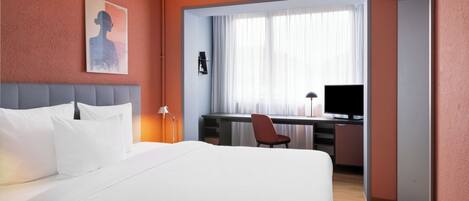 Una habitación de hotel con cama, escritorio y silla, televisor y ventana con cortinas.