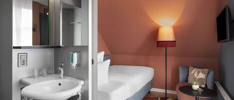 A modern bathroom with a white sink, mirror, and a sofa bed with pillows.