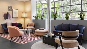 A modern living room with a sofa, armchairs, a coffee table, and a large window with plants. - Hotel La Pergola (Bern)