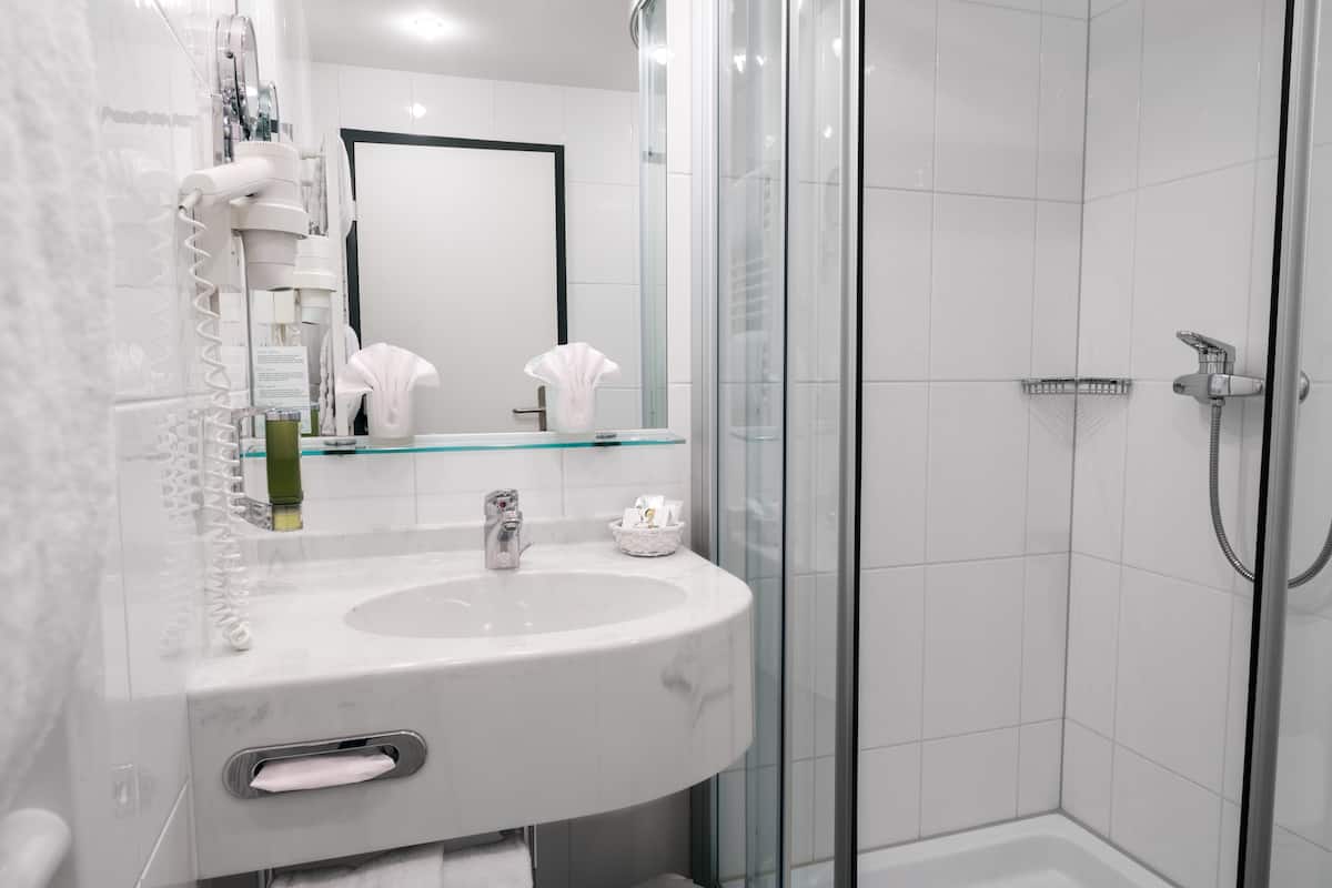 Un baño moderno con cabina de ducha de vidrio, un lavabo blanco con encimera de mármol y un espejo grande.