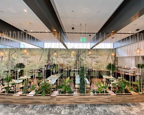Un vaste espace intérieur aménagé avec différents coins salon, un escalier central et des plantes suspendues.