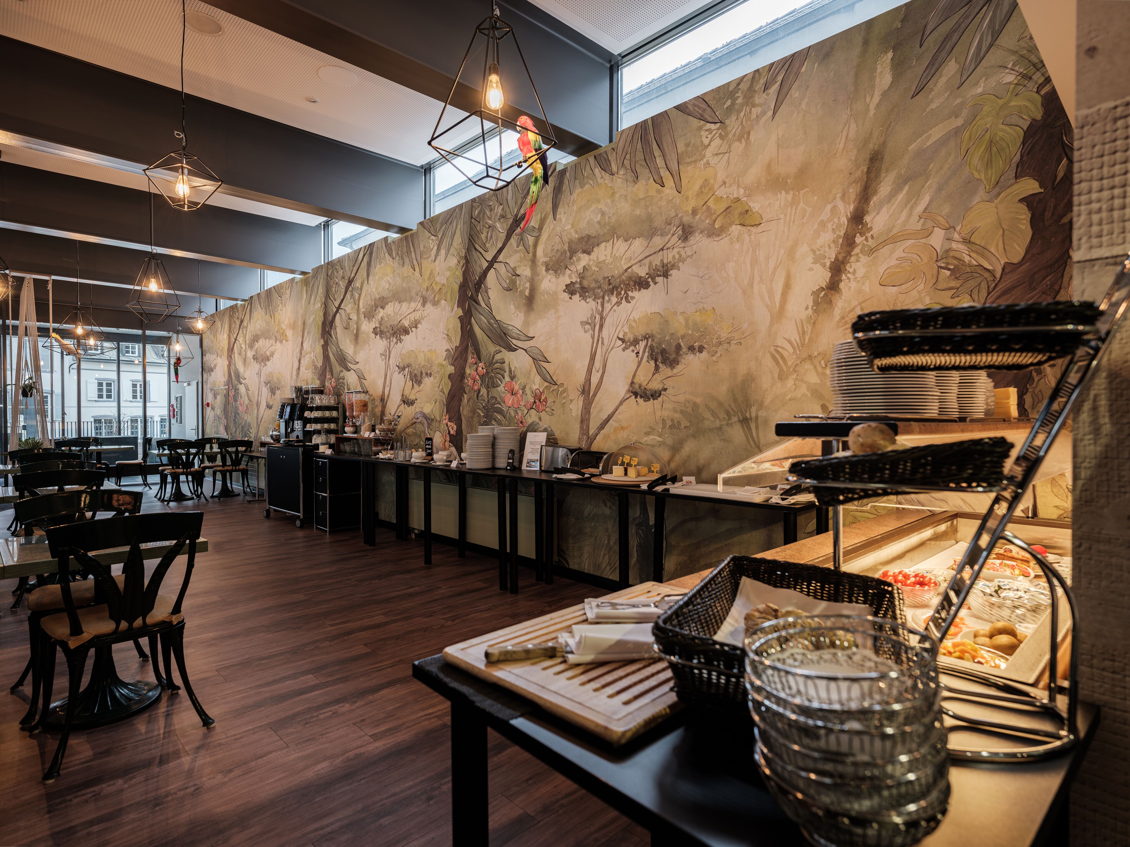 A restaurant with wooden flooring, a buffet counter, and a mural of trees and flowers on the wall.