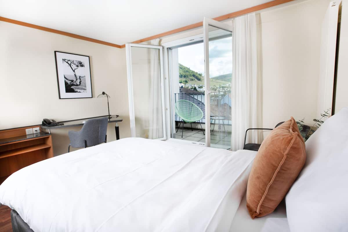 Habitación de hotel con cama, escritorio, silla y balcón con vista al paisaje.