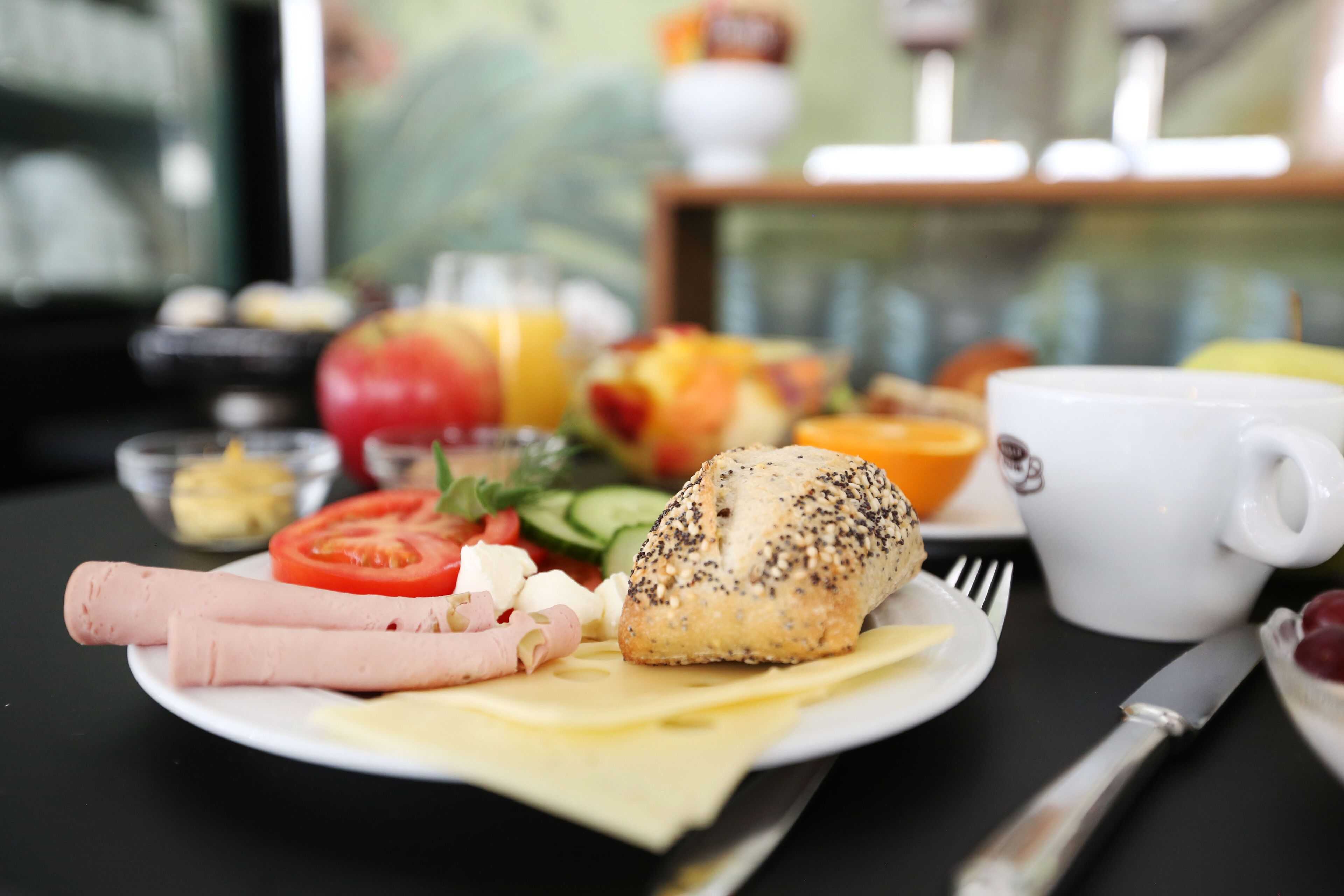 Ein Frühstücksteller mit Schinken, Käse, einem Mohnbrötchen und Gemüse.