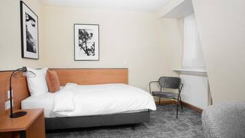 Une chambre d’hôtel avec un lit, un bureau, une chaise et deux tableaux encadrés au mur.