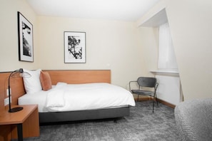 Una habitación de hotel con una cama, un escritorio, una silla y dos cuadros en la pared.