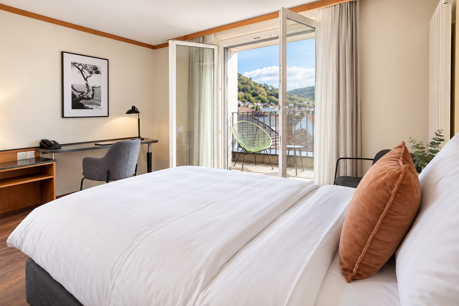 Habitación de hotel con cama, escritorio, silla y ventana grande con vista a una colina.