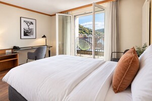 Habitación de hotel con cama, escritorio, silla y ventana grande con vista a una colina.