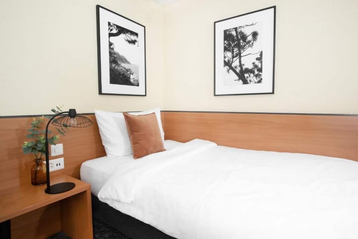 Habitación de hotel con cabecera de madera, ropa de cama blanca, lámpara de noche y dos fotografías en blanco y negro enmarcadas en la pared.