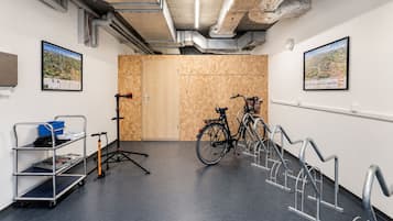 Una habitación con una puerta de madera, una bicicleta, un carro metálico con objetos y un soporte para bicicletas en la pared.