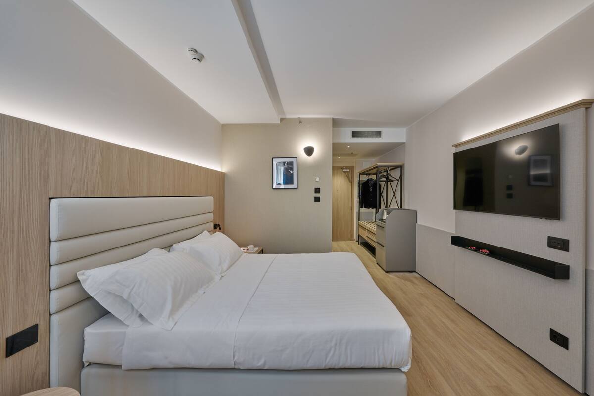 Una habitación de hotel moderna con una cama grande, un televisor de pantalla plana en la pared y un vestidor.