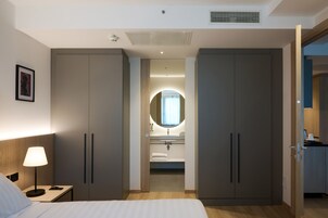 Habitación de hotel con cama, mesita de noche, lámpara, armario y baño con lavamanos y espejo.