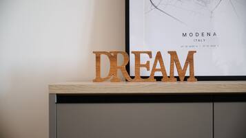 Letras de madera que deletrean "DREAM" sobre una superficie de madera, con un mapa enmarcado de Módena, Italia, al fondo.