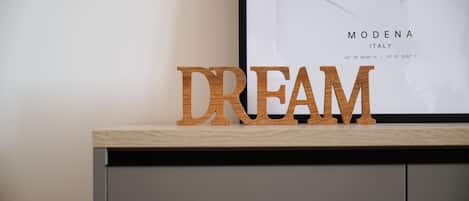 Letras de madera que deletrean "DREAM" sobre una superficie de madera, con un mapa enmarcado de Módena, Italia, al fondo.