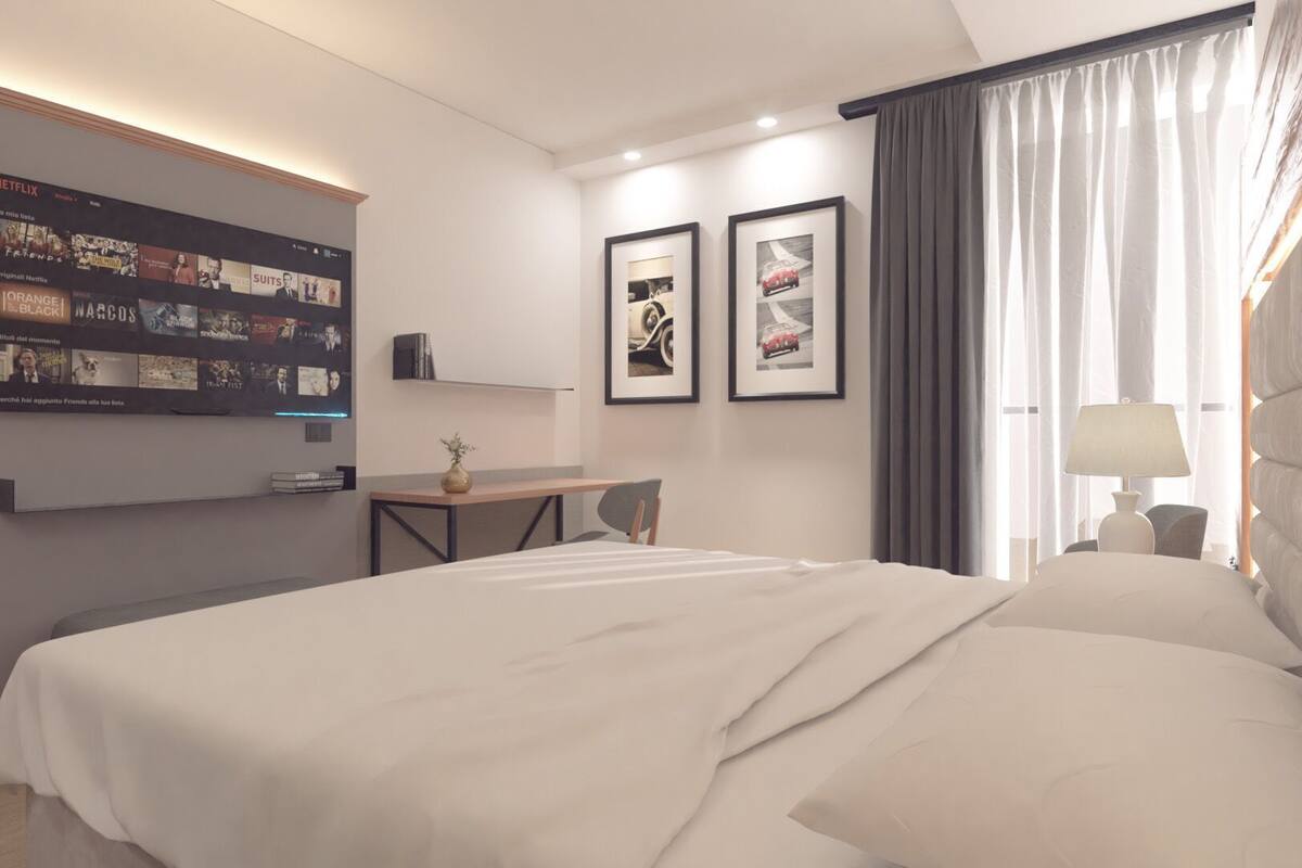 Habitación de hotel moderna con una cama grande, un escritorio, un televisor de pantalla plana montado en la pared y dos cuadros enmarcados.