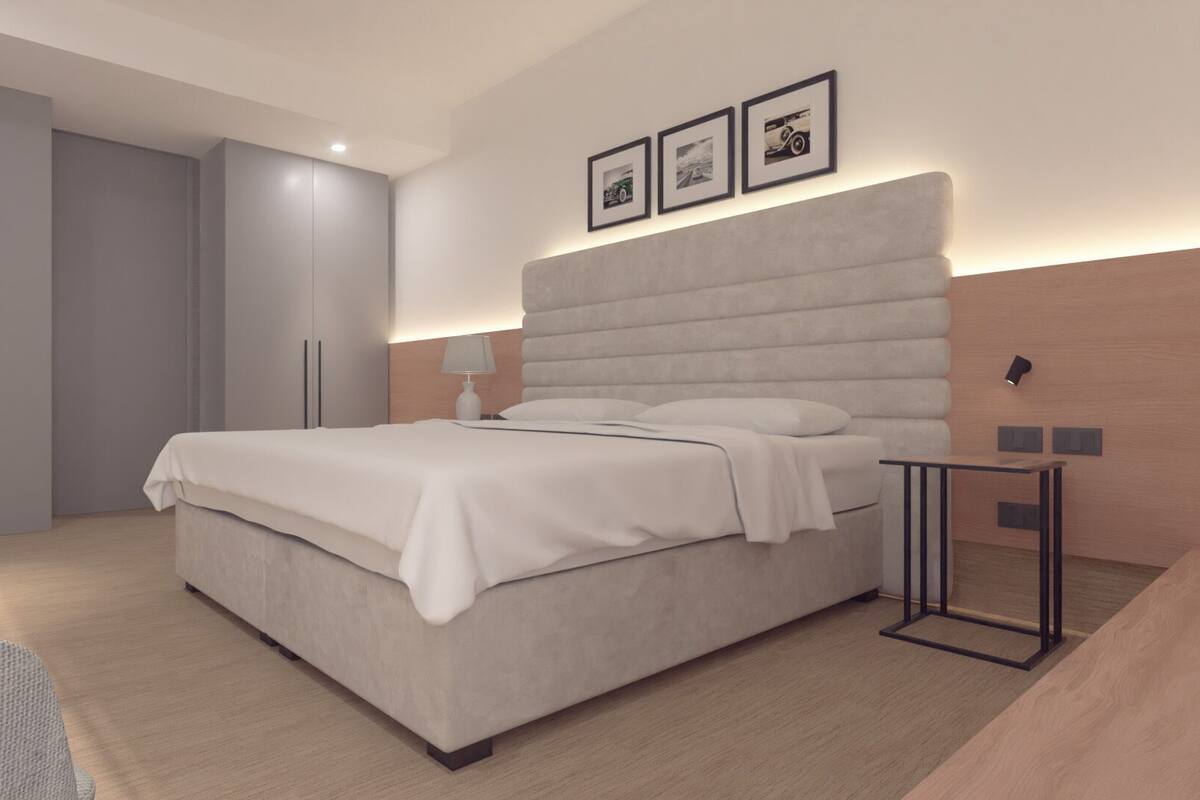 Un dormitorio moderno con una cama grande, un armario gris, mesitas de noche y cuadros enmarcados en la pared.