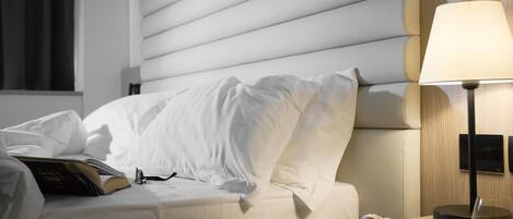 A neatly made bed with white linens, a bedside table with a lamp, a book, and a plate with croissants and orange juice.