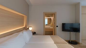A hotel room with a large bed, a bedside table with a lamp, a TV, and a bathroom visible through an open door.