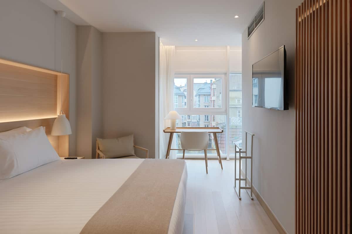 Ein modernes Hotelzimmer mit einem großen Bett, einem Schreibtisch und einem an der Wand befestigten Fernseher.