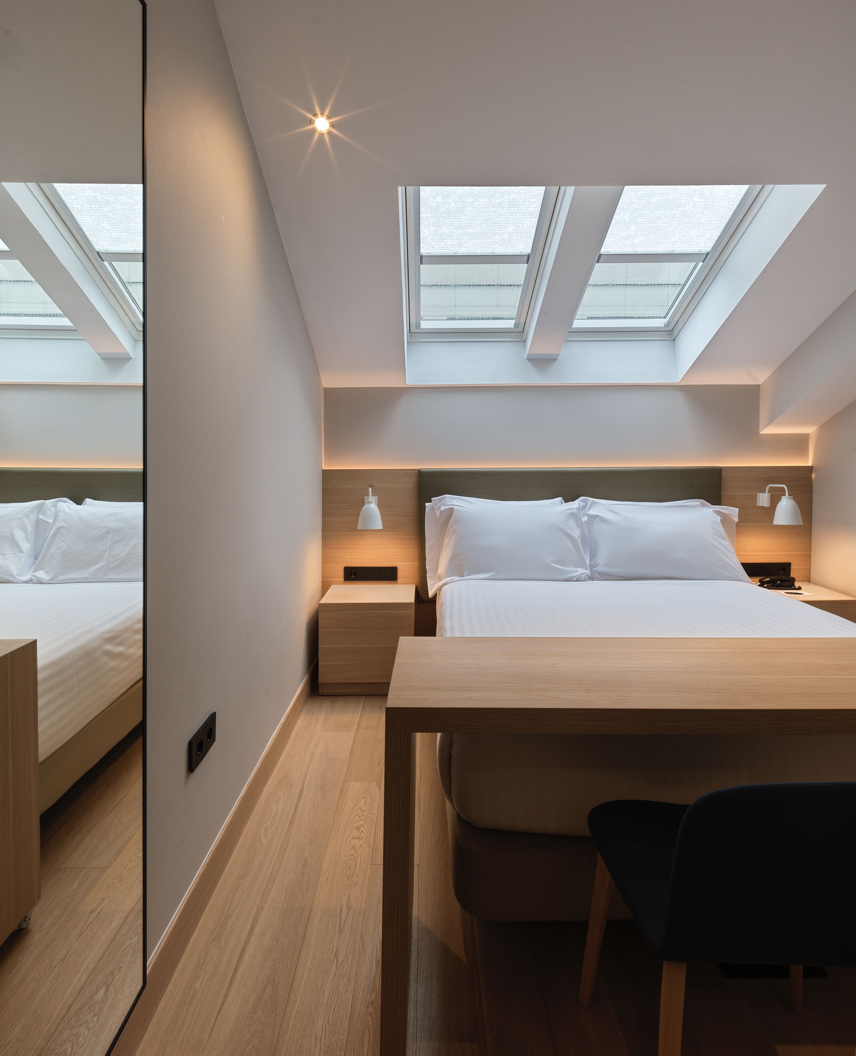 Een moderne slaapkamer met dakramen, een bed, nachtkastjes en een bureau.