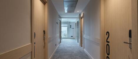 Un pasillo moderno de hotel con pisos alfombrados, puertas de madera e iluminación empotrada en el techo.