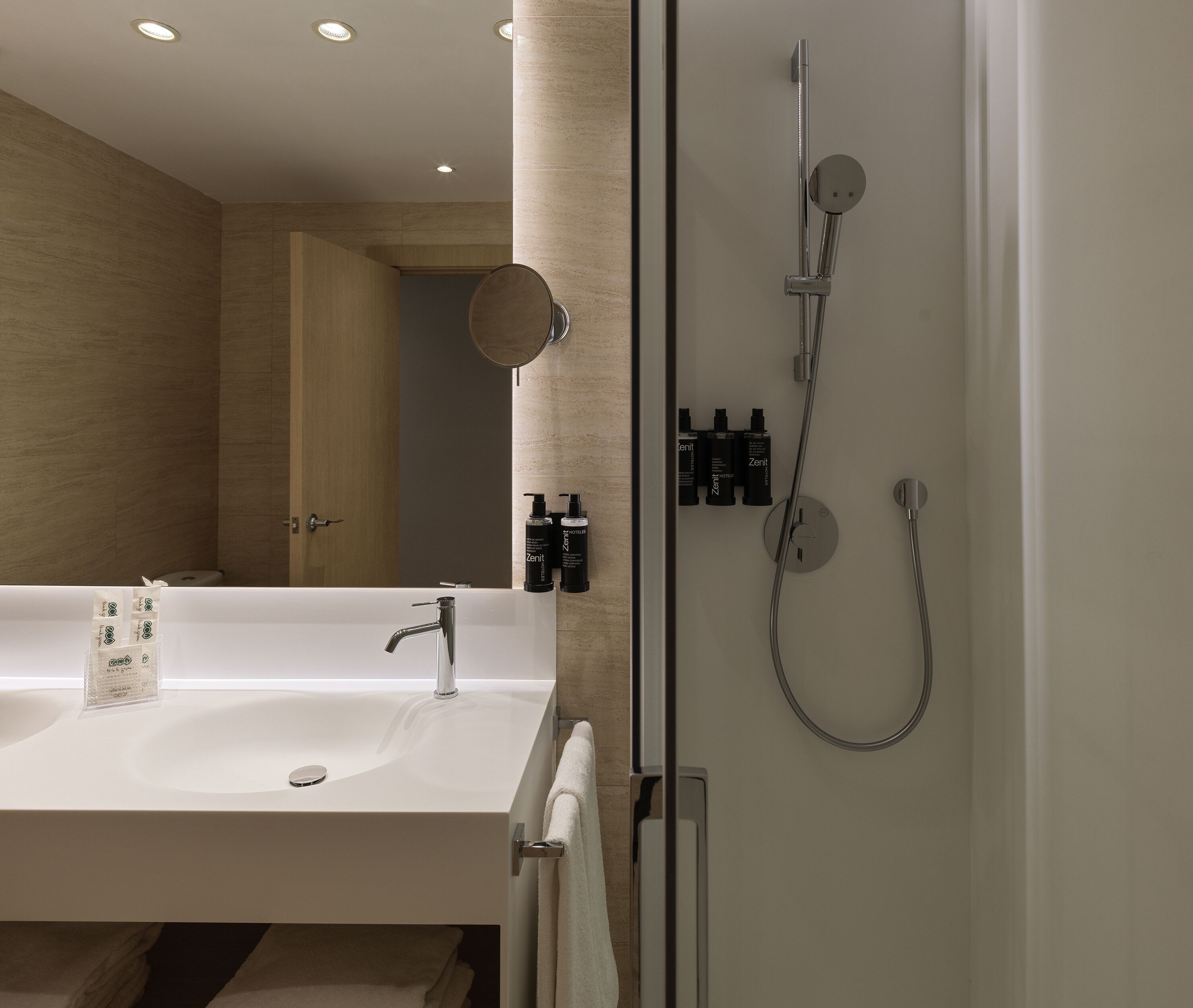 Un baño moderno con un lavamanos grande, cabina de ducha con mampara de vidrio y artículos de aseo en la pared.