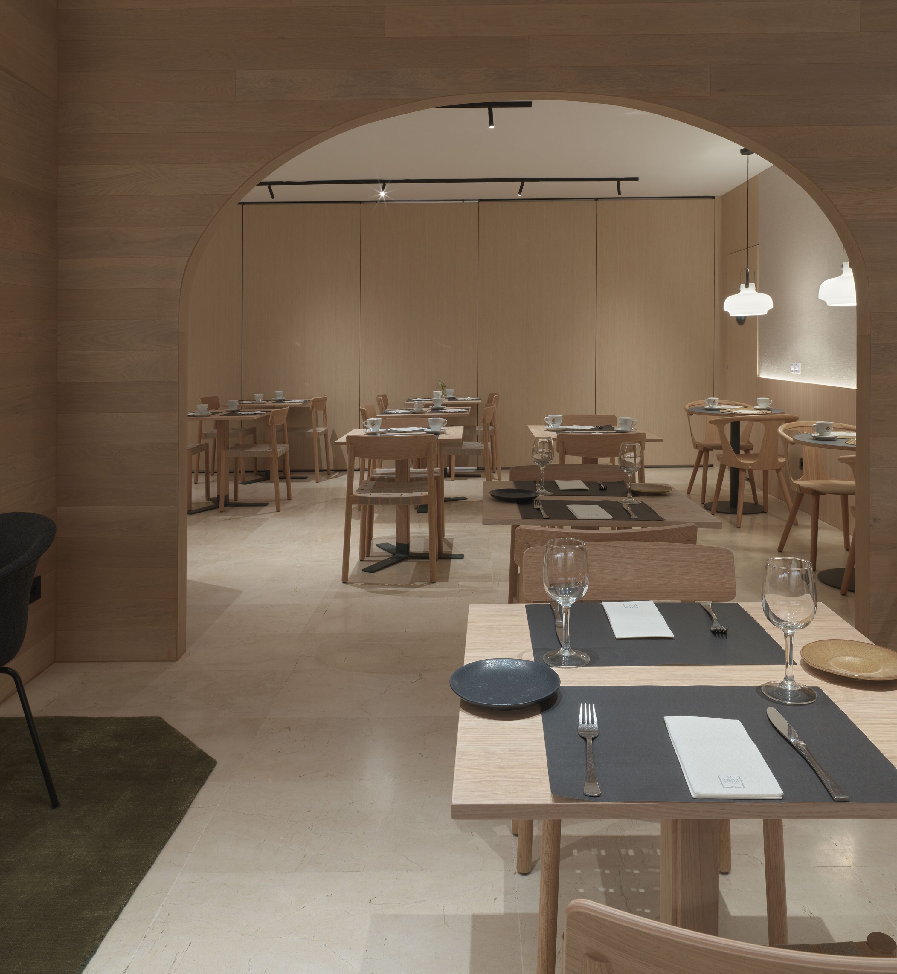 A modern dining area with wooden tables and chairs, a green carpet, and a wooden archway.
