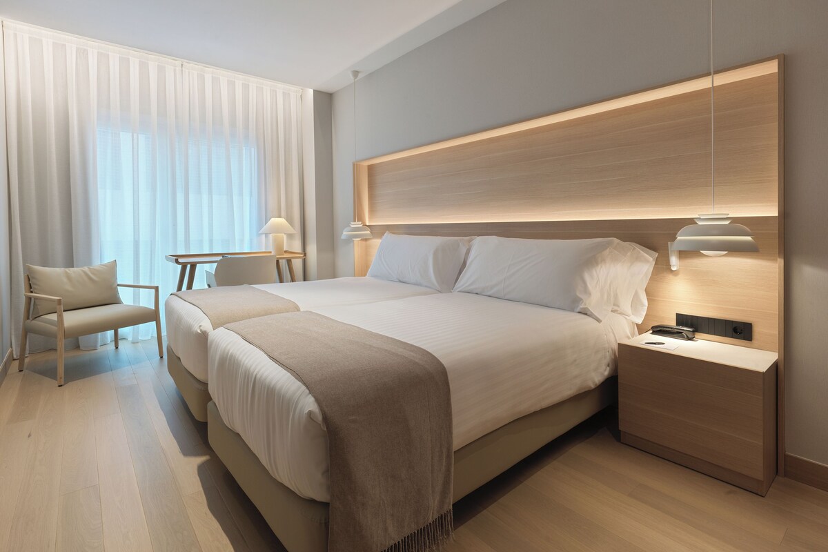 A modern hotel room with a large bed, bedside tables, a desk, and a chair.