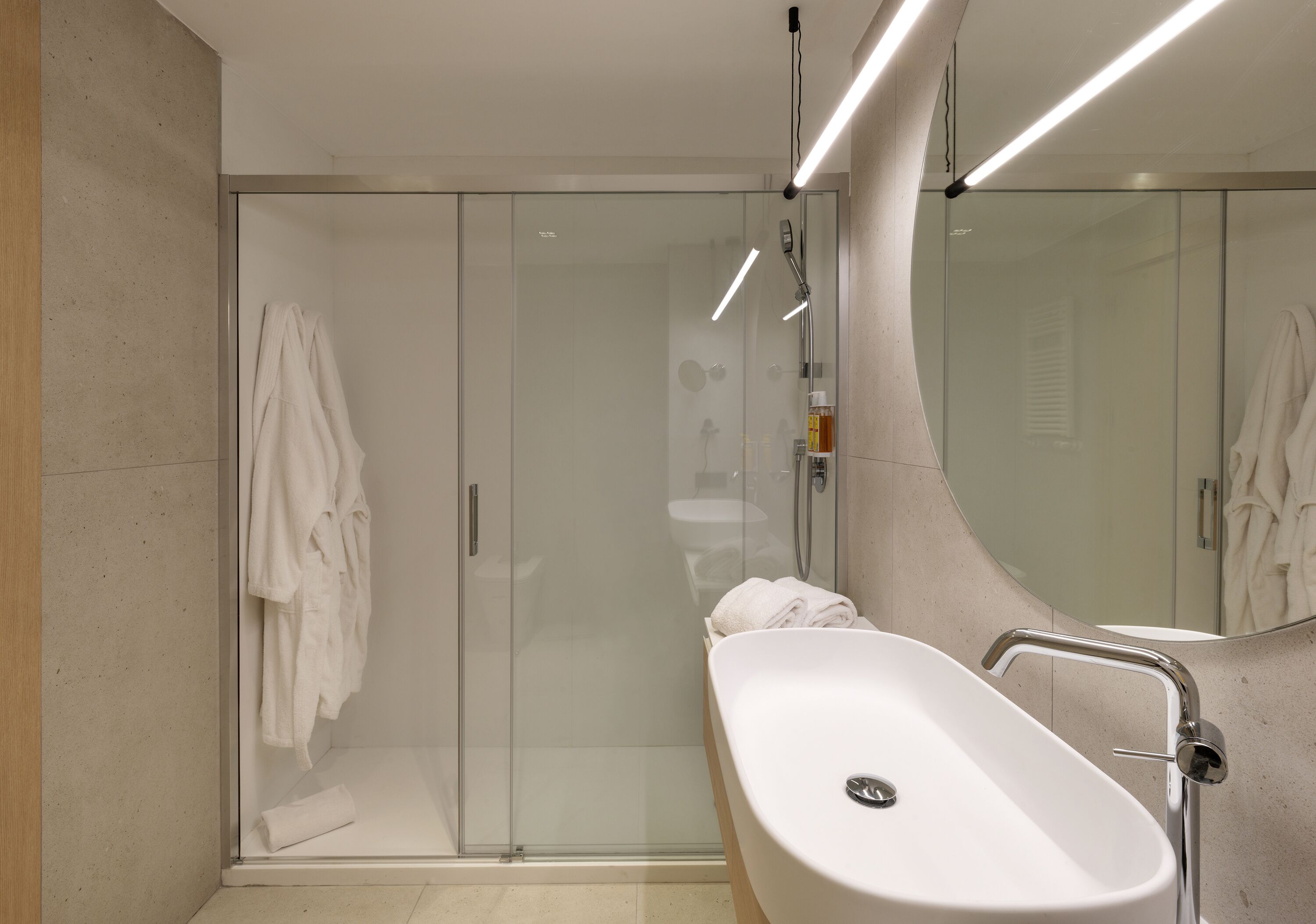 A modern bathroom with a glass-enclosed shower, a white sink, and a large mirror.