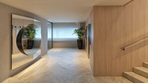 Un pasillo moderno con una escalera de madera, un espejo circular y dos plantas en macetas.