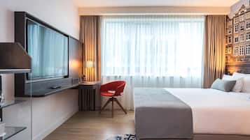 Una habitación de hotel con cama, escritorio con silla, televisor y un ventanal con cortinas.