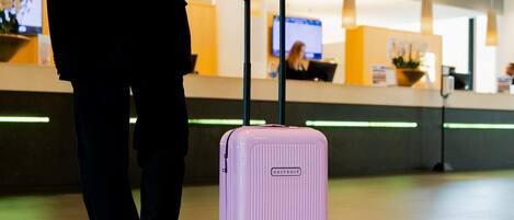 Een persoon met een roze koffer in een moderne lobby met een receptiebalie en een televisiescherm.