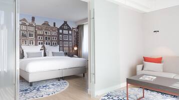 Una habitación de hotel moderna con una cama, un sofá, una mesita de centro y vistas a un paisaje urbano a través de un ventanal.