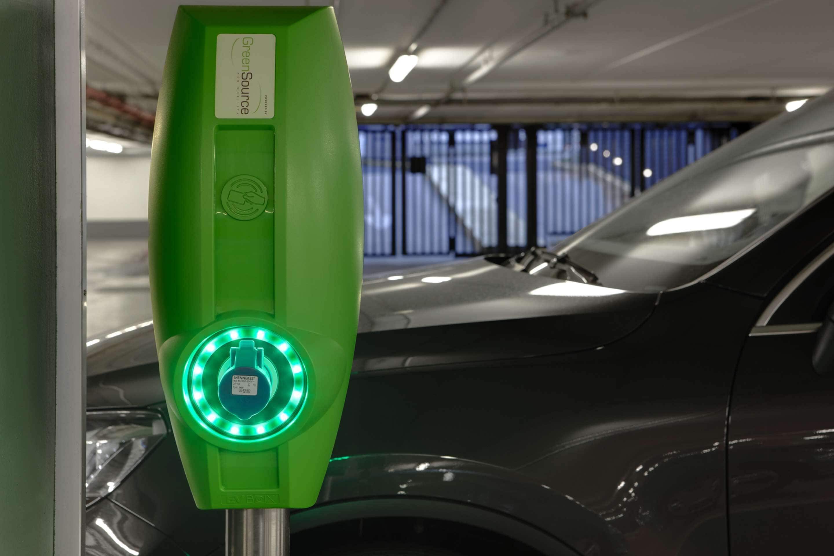 Una estación de carga para vehículos eléctricos verdes con un rótulo que dice "Green Source" y un coche estacionado cerca.